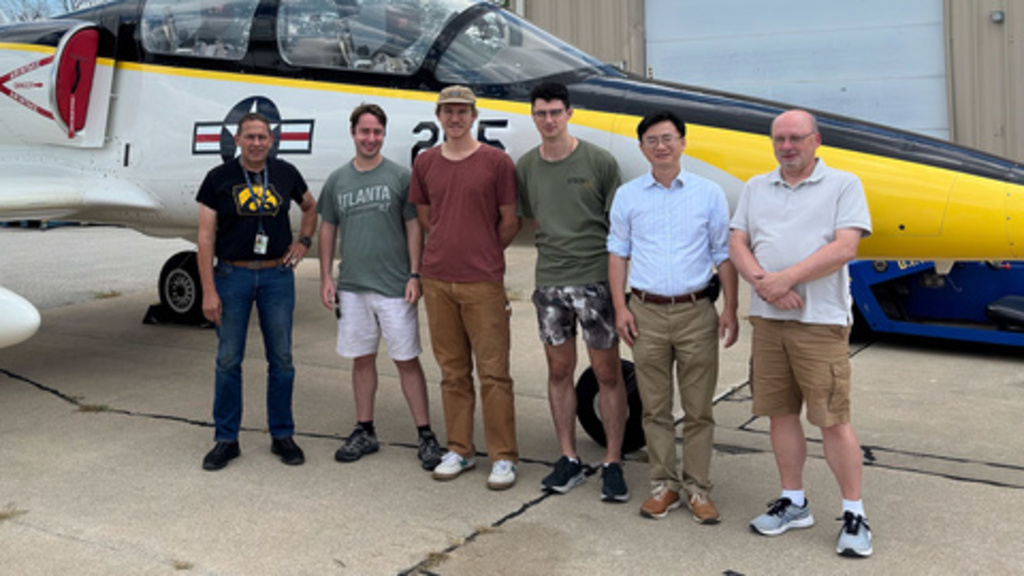 Six people pose in front of a jet